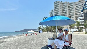 A beach with a clear sky, a sandy shore, and a few umbrellas. - Suite deluxe with private Jacuzzi and ocean view. (Santa Marta)