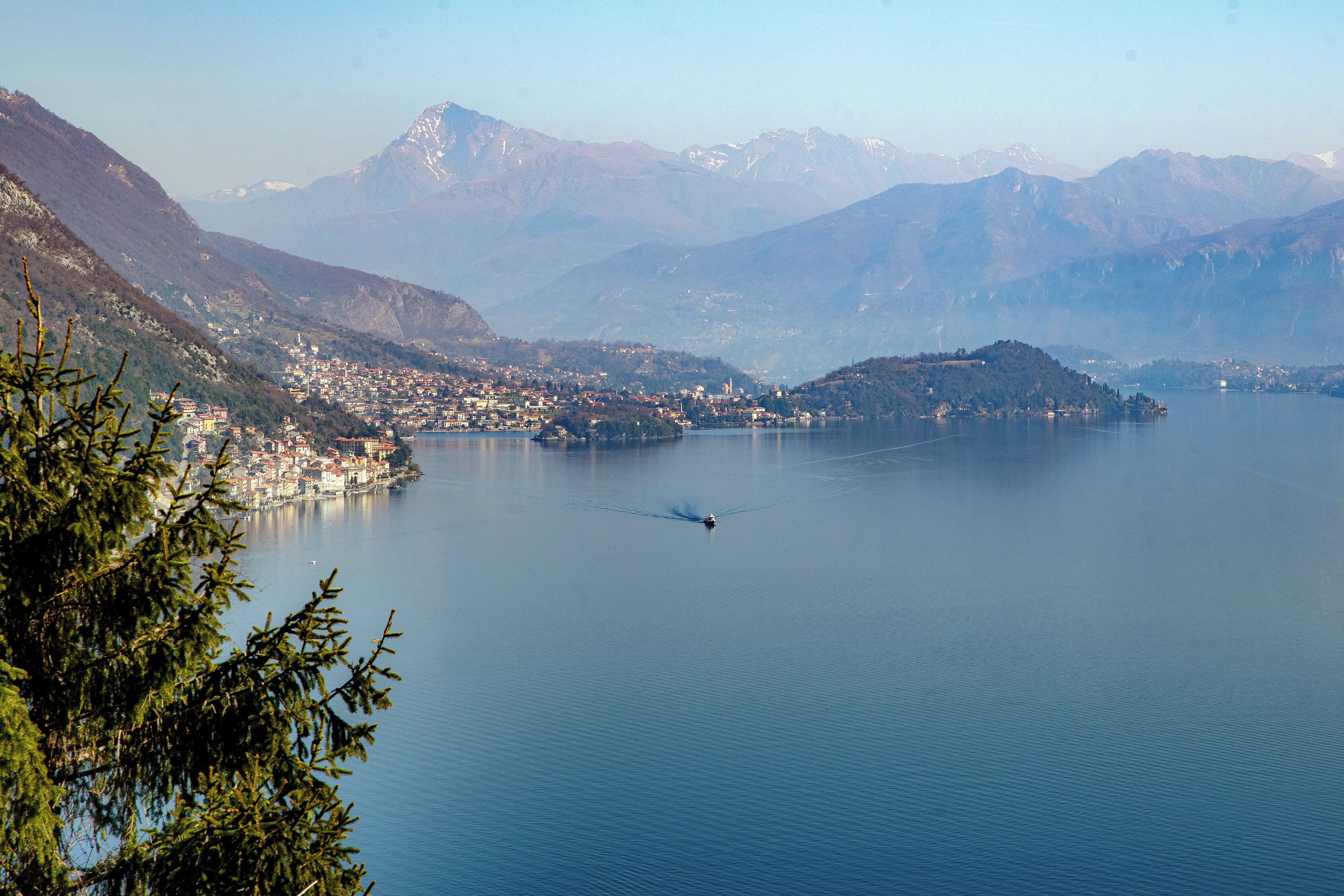 A helicopter flying over a calm lake with a mountainous backdrop and a town on the shore.