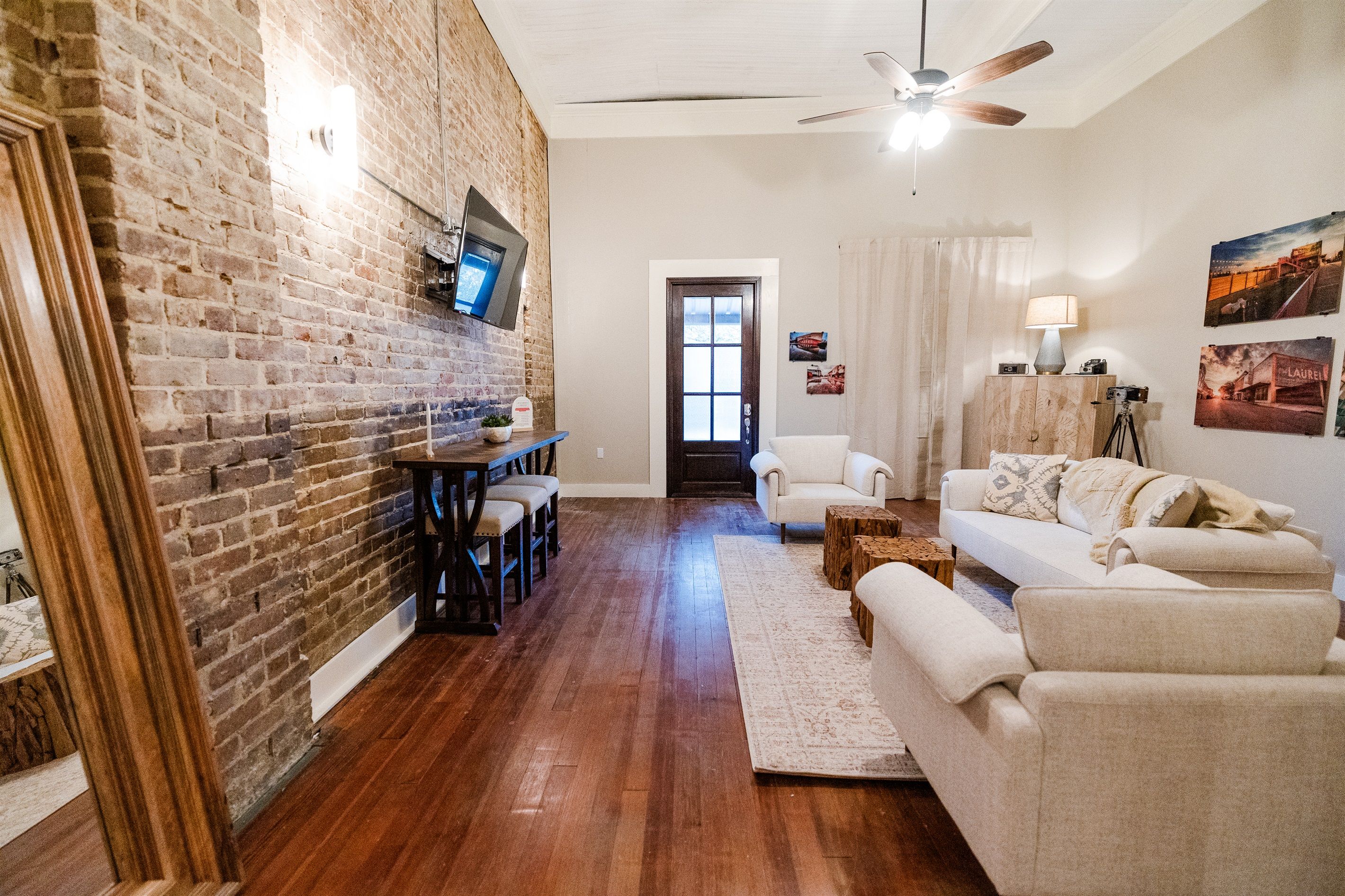 A living room with a brick wall, wooden floor, white furniture, and a ceiling fan.