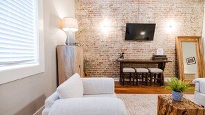 Un salon avec un mur en briques, un téléviseur à écran plat, une table basse en bois et un canapé.