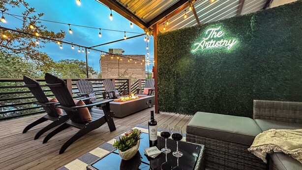 Une terrasse extérieure avec des fauteuils Adirondack, un foyer et une table avec des verres à vin.