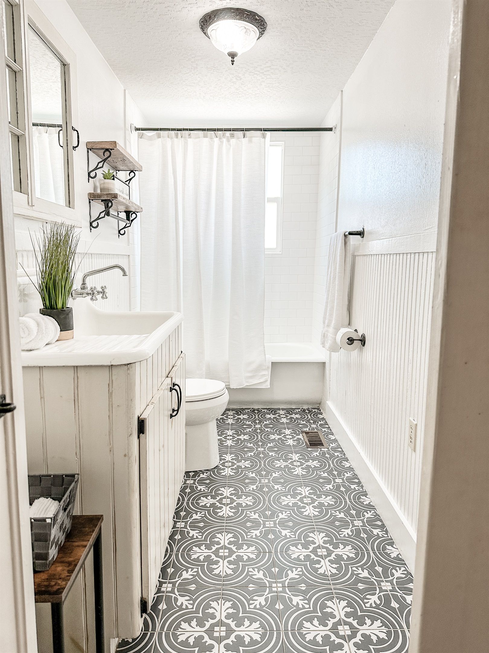 Ein schmales Badezimmer mit einem weißen Waschbecken, einer Toilette und einer Badewanne. Der Boden ist mit einem Muster versehen und es gibt eine Deckenleuchte.