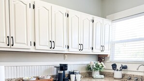 A modern kitchen with white cabinetry, a granite countertop, a built-in dishwasher, and a window with blinds. - Centrally Located Downtown, Full Kitchen, Patio (Laurel)