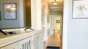 A hallway with a wooden floor, a white decorative cabinet with a mirror, and framed artwork on the walls. - Centrally Located Downtown, Full Kitchen, Patio (Laurel)
