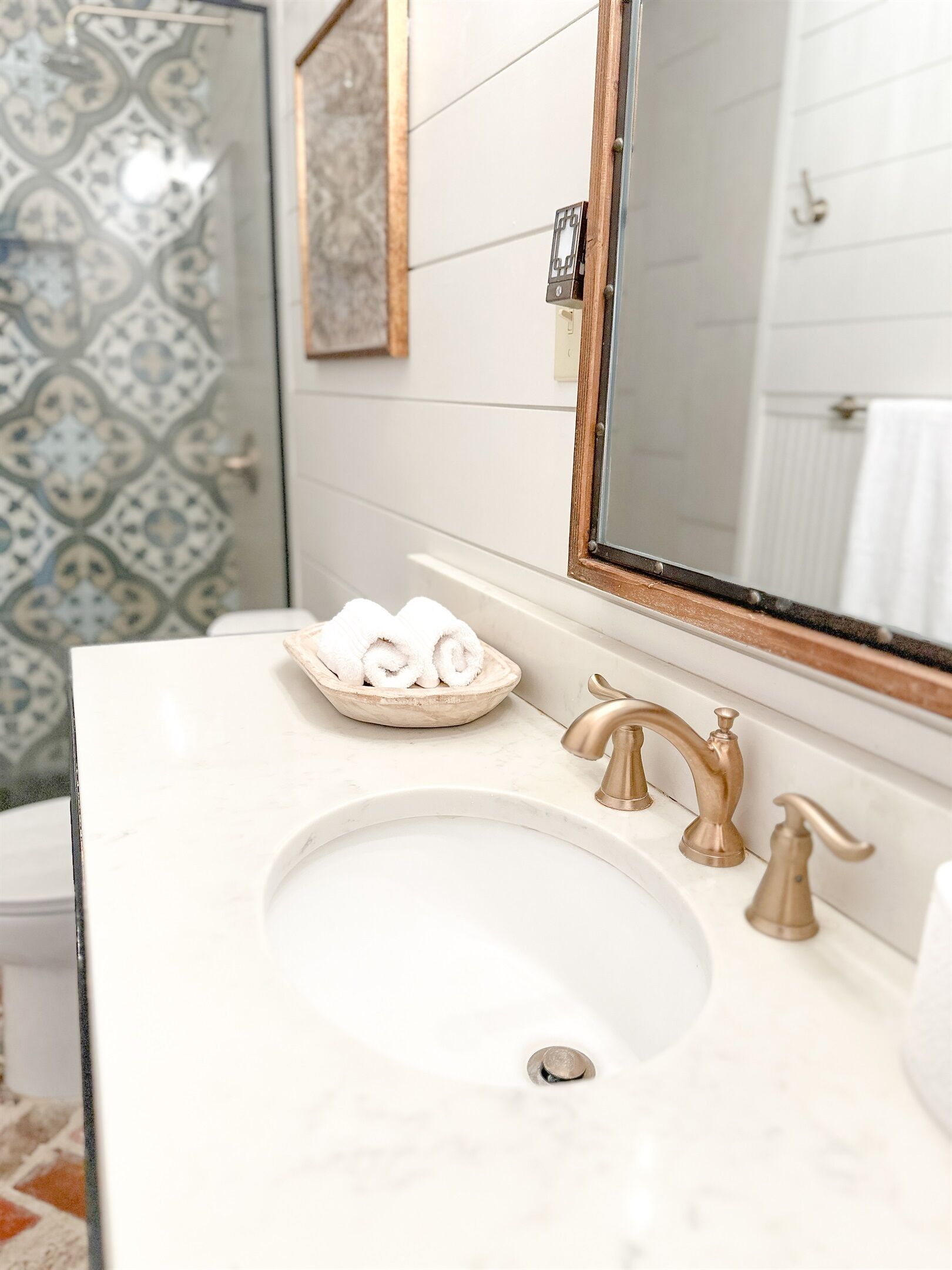 A bathroom with a white sink, a bowl of rolled towels, and a mirror with a wooden frame.
