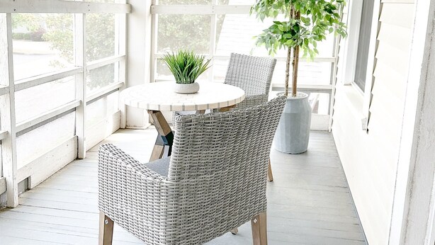 Une véranda avec une table ronde, des chaises en osier, une plante en pot et un ventilateur de plafond.