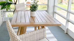 Een houten tafel met een plantje, omringd door rieten stoelen, in een kamer met grote ramen.