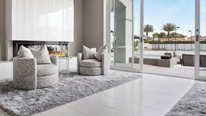 Ein modernes Wohnzimmer mit Kamin, zwei gemusterte Sessel, einem flauschigen Teppich und einer Glastür zu einer Außenpatio mit Pool.