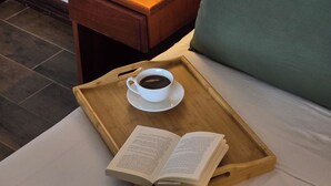 Una cama bien hecha con un almohárraga verde, una mesita de noche con una lámpara, y una bandeja con una taza de café y un libro abierto.