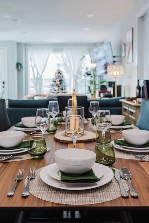 Una mesa puesta para una comida, con platos blancos, servilletas verdes y copas de cristal.