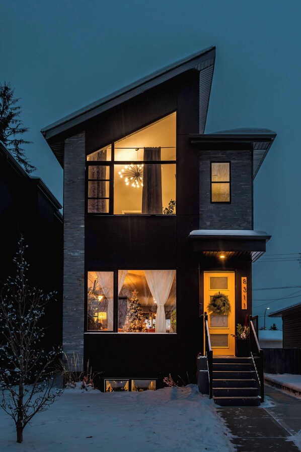 Una casa moderna de dos pisos con ventanas grandes, una escalera visible y suelo cubierto de nieve.