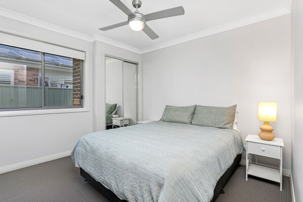 A bedroom with a bed, a nightstand, a lamp, a ceiling fan, and a window.