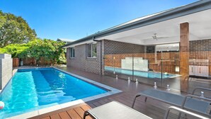 A modern backyard with a swimming pool, wooden deck, and a covered patio area.