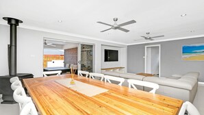 A modern living room with a wooden dining table, white sofas, and ceiling fans.