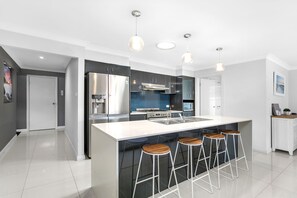 A modern kitchen with a central island, bar stools, stainless steel appliances, and pendant lighting.