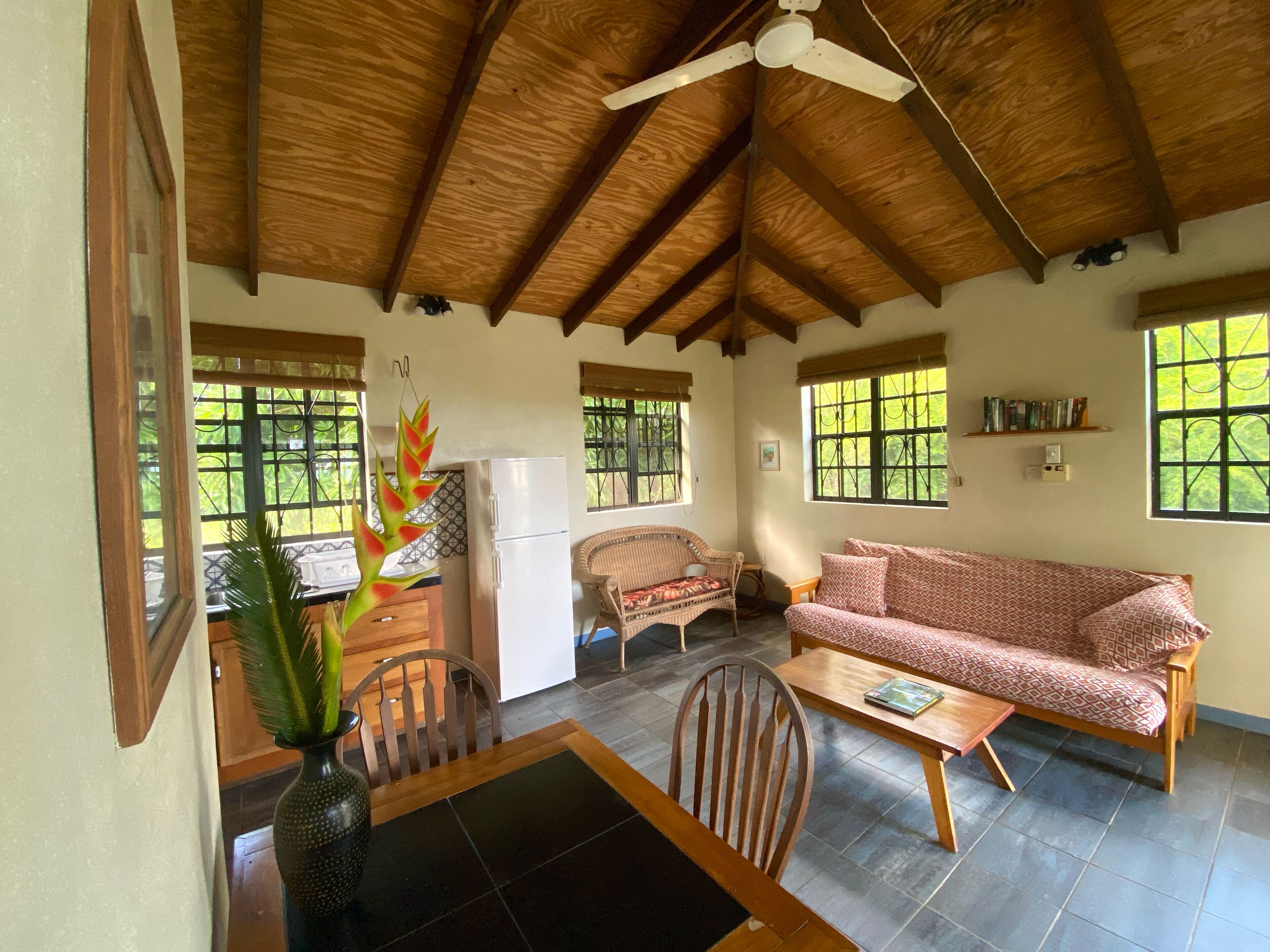 Una habitación acogedora con techo de madera, una mesa de comedor con sillas, un sofá, un refrigerador y una ventana con vistas a zonas verdes.