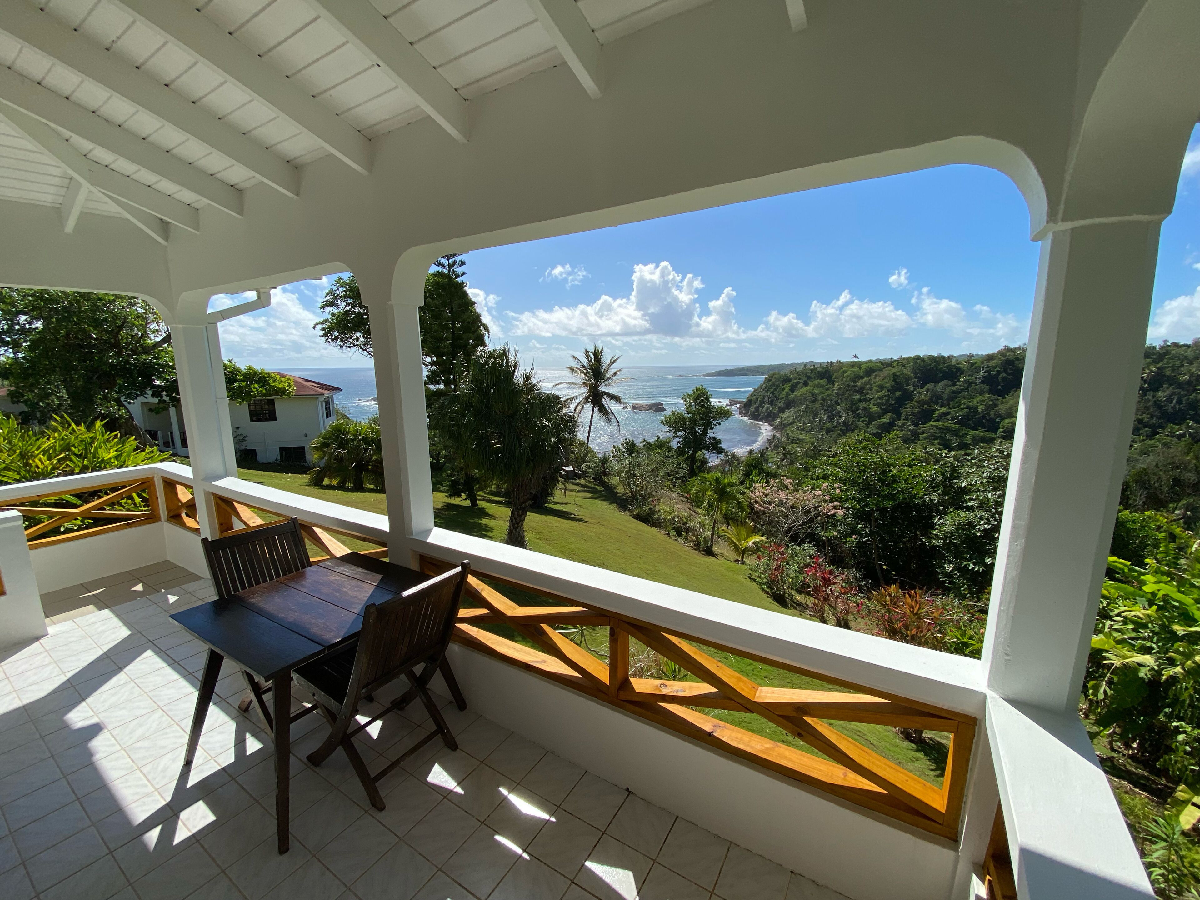Un área de estar al aire libre con techo, que cuenta con una mesa y sillas, con vista a un paisaje exuberante de árboles y el océano.