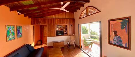 A spacious living area with a wooden ceiling, a ceiling fan, a sofa, a coffee table, and a bookshelf.