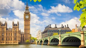 Vista delle case del Parlamento e del Big Ben a Londra, con il Tamigi in primo piano e un ponte verde sullo sfondo.