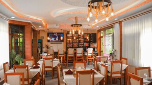 A restaurant with wooden tables and chairs, a bar area, and a television screen. - River House Lodge  (Arusha)
