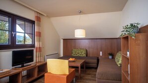 A cozy living room with a television, wooden furniture, a dining table, and a large window with curtains.