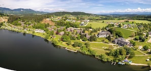 Vista aérea de uma vila à beira do lago, com casas, um prédio grande e um cais com barcos.