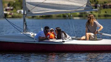 A sailboat with a family of four, including a child in a life jacket, on a calm body of water.