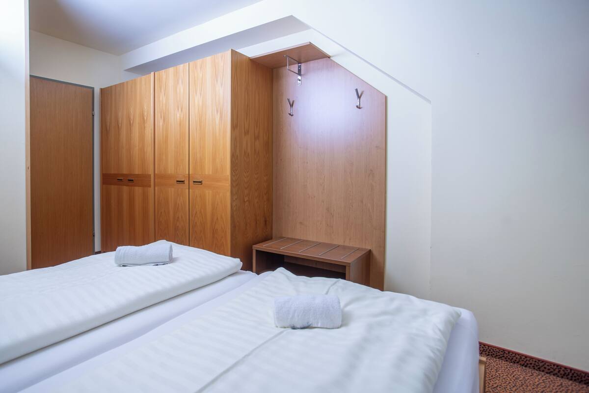 Une chambre avec deux lits, des armoires en bois, une petite table de chevet et un plafond en pente.