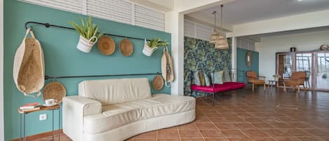 A spacious living area with a white sofa, a small table, and a red chair. There are several potted plants and woven baskets on the wall.