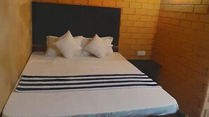 A room with a brick-patterned wall, a wooden bed with a dark headboard, and a wall-mounted light fixture. - Superb 2-bedroom villa in Mirissa (Mirissa)