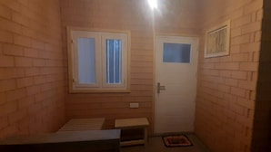 A small, dimly lit room with brick walls, a single window with curtains, a door, and a small bench. - Superb 2-bedroom villa in Mirissa (Mirissa)