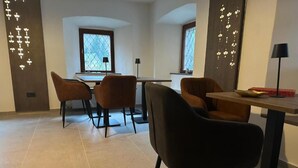 A modern dining area with a table and chairs, a window with a view, and decorative wall lighting. - 4 Elements Resort Bled Studio with sofa bed (Radovljica)