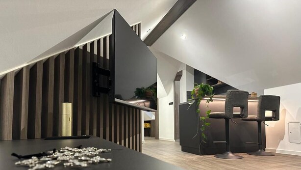 A modern kitchen with a dark countertop, wooden paneling, and a built-in stove. There are two black chairs and a potted plant in the background. - 4 Elements Resort Bled Studio with sofa bed (Radovljica)