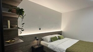 A modern bedroom with a bed, bedside table, and a wall-mounted shelf with a plant. - 4 Elements Resort Bled Studio with sofa bed (Radovljica)