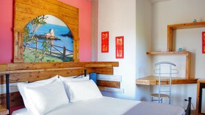 Un dormitorio con cabecera de madera, una cama con ropa de cama blanca, un cuadro de una escena costera y un pequeño estante de madera con objetos decorativos.