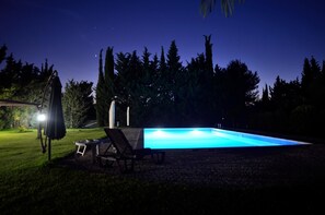 Piscina à noite com espreguiçadeiras e área coberta.