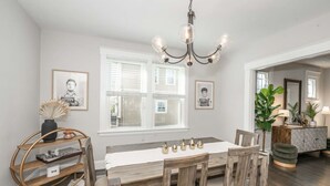 A dining area with a wooden table, chairs, a chandelier, and a sideboard with plants. - StayDelta | Hyde Park (Cincinnati)