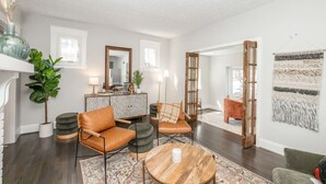 A modern living room with a sofa, ottomans, a coffee table, and a patterned rug. There is a sideboard with decorative items and a mirror. - StayDelta | Hyde Park (Cincinnati)