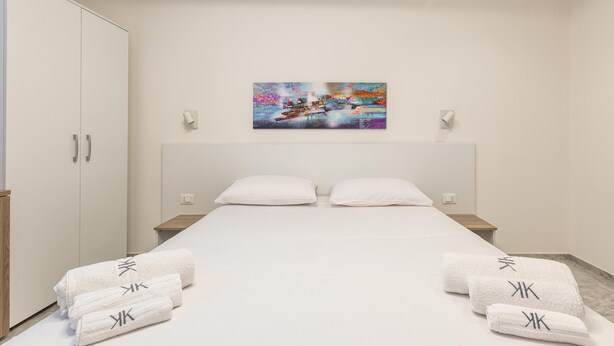 A hotel room with a bed, white towels with a logo, a painting on the wall, and a wardrobe. - Krono Relais - Camera Matrimoniale (Gallipoli)