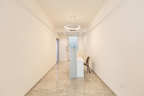 A hallway with a marble floor, a white reception desk, and a door at the end. - Krono Relais - Camera Matrimoniale (Gallipoli)
