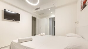 A modern hotel room with a large bed, a flat-screen TV mounted on the wall, and a door leading to a bathroom. - Krono Relais - Camera Matrimoniale (Gallipoli)