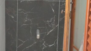 Ducha con azulejos de mármol oscuro y un marco de puerta de madera.