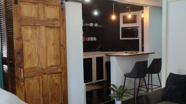 Una cocina compacta con barra, armarios de madera y dos taburetes negros.