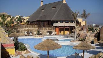 A resort with a large pool, thatched umbrellas, and a building with a dark roof.