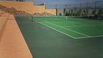 Una cancha de tenis con red, rodeada por un muro bajo y un muro de piedra.