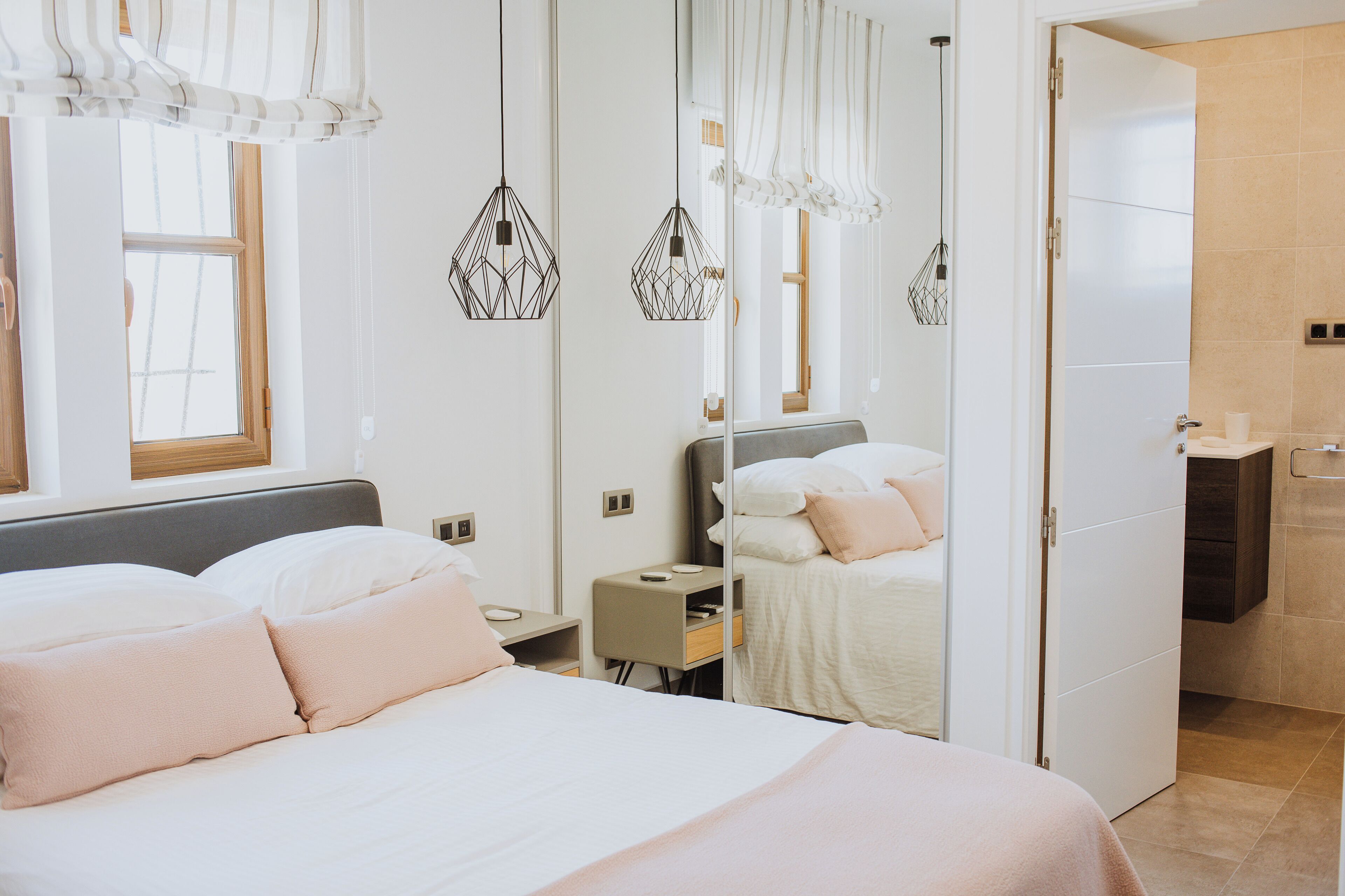Ein modernes Schlafzimmer mit einem großen Bett, Nachttischen, einem Spiegel und einem durch eine offene Tür einsehbaren Badezimmer.