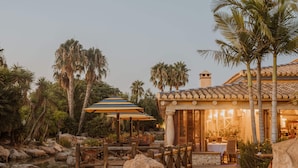 Un restaurante con terraza, palmeras y un sendero de piedra.