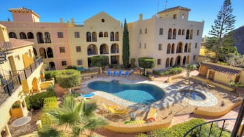 Um pátio com piscina, espreguiçadeiras e um edifício com várias varandas e arcos.