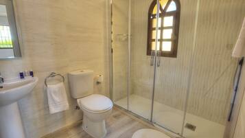 Un baño moderno con ducha envuelta en vidrio, inodoro, lavamanos y un perchero para toallas.