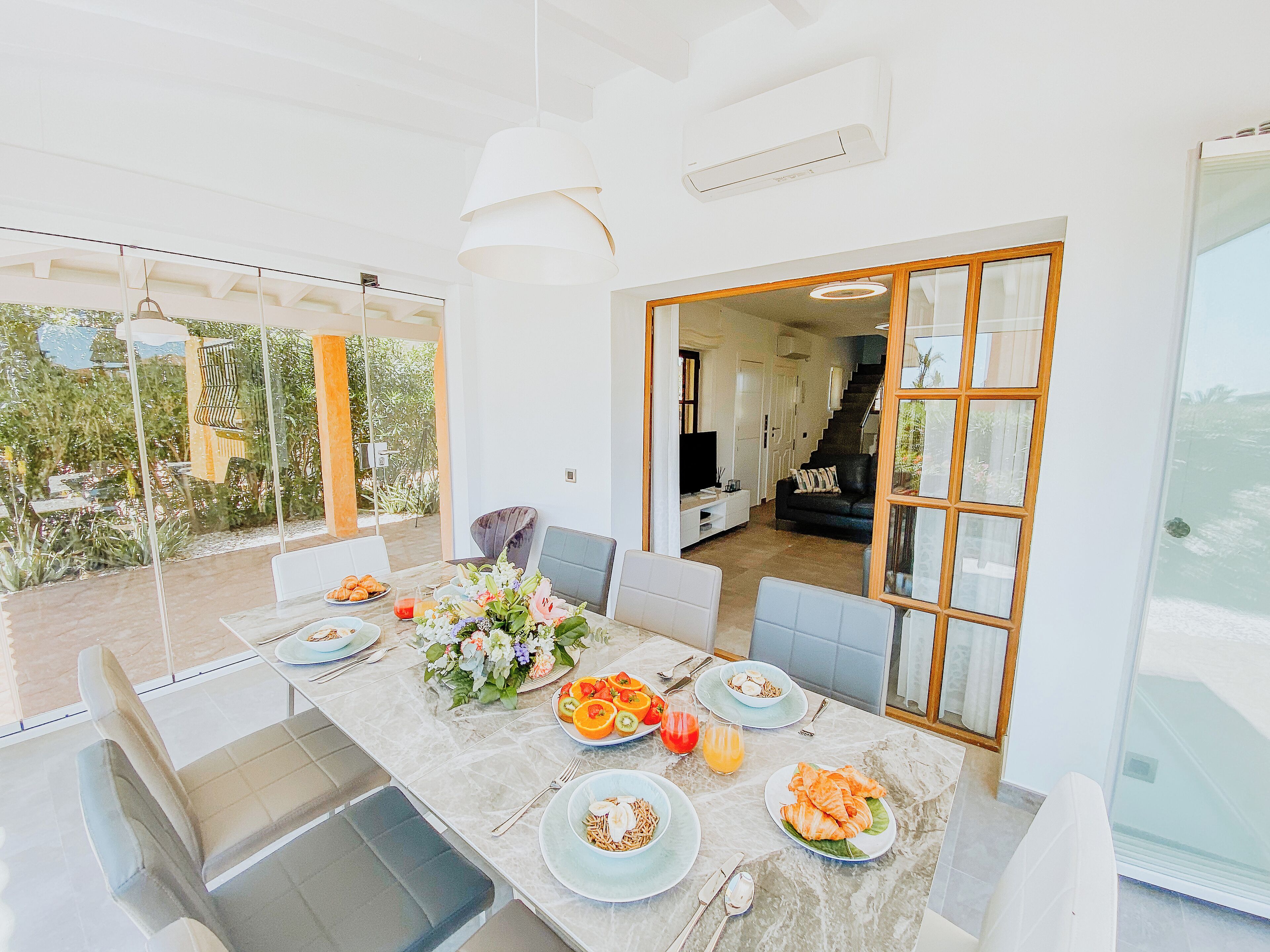 A dining area with a marble table set for a meal, a sofa, and a TV in the background.